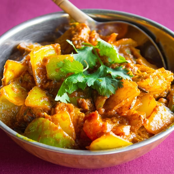 Indian curry with bell peppers and cilantro in a metal serving bowl with a spoon.