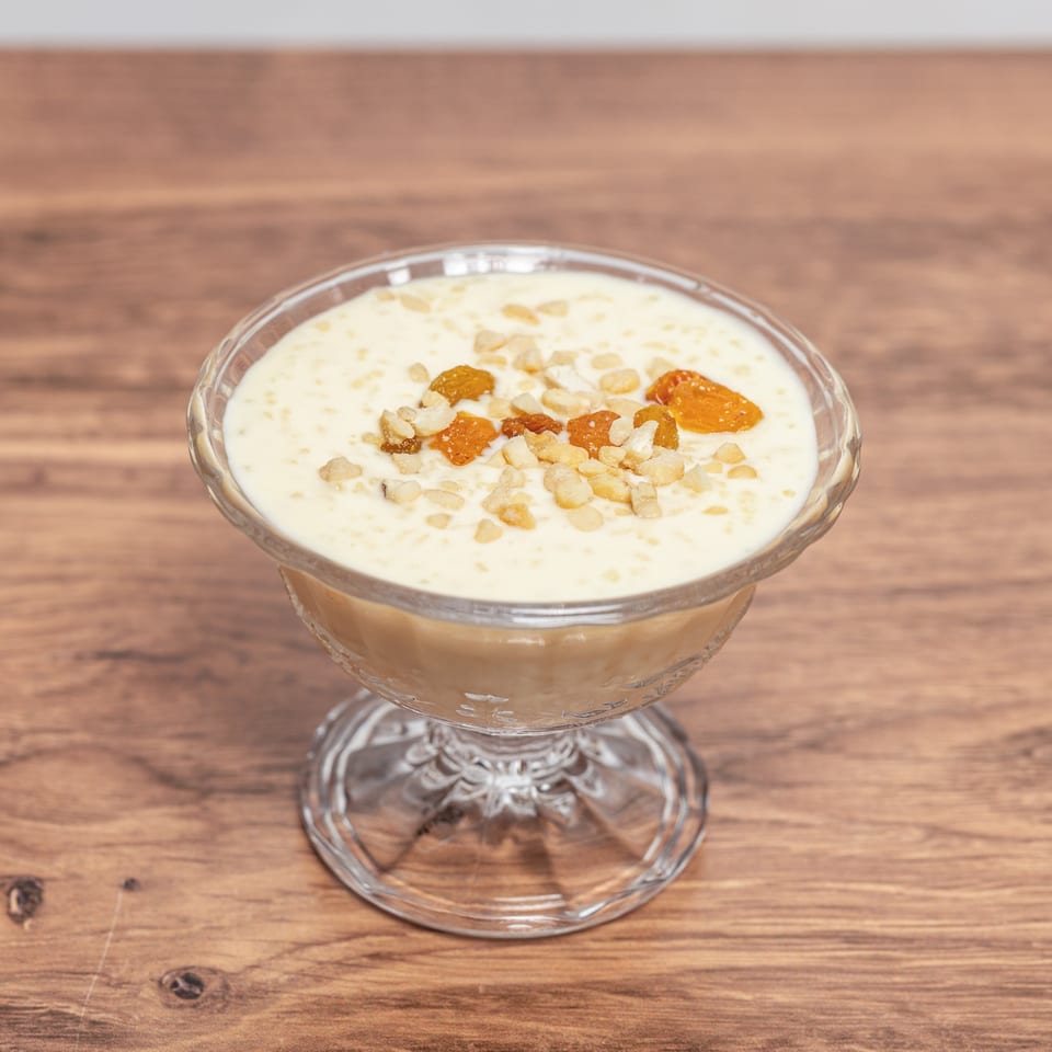 Creamy pudding topped with chopped nuts and golden raisins in a glass dessert bowl on a wooden table.