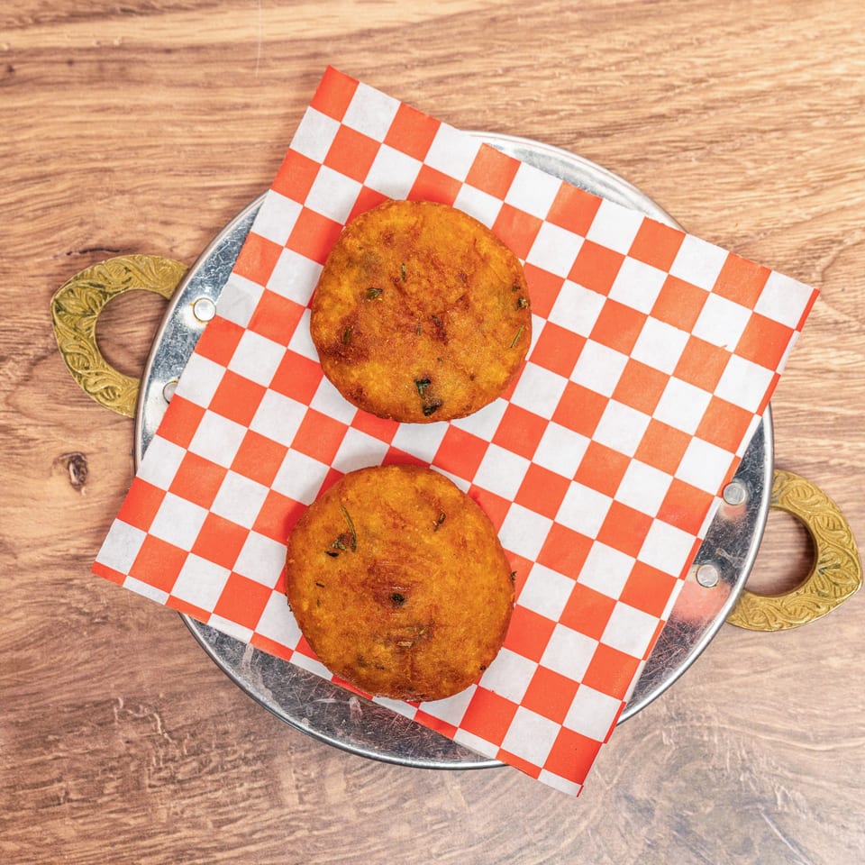 Two golden fried savory patties on red-and-white checkered paper in an ornate metal tray atop a wooden table.