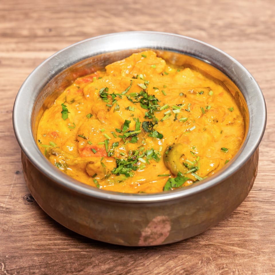 Creamy orange curry garnished with fresh cilantro in a metal bowl on a wooden table.