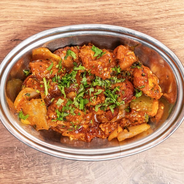 Metal serving dish filled with saucy roasted vegetables and paneer, garnished with fresh cilantro on a wooden table.