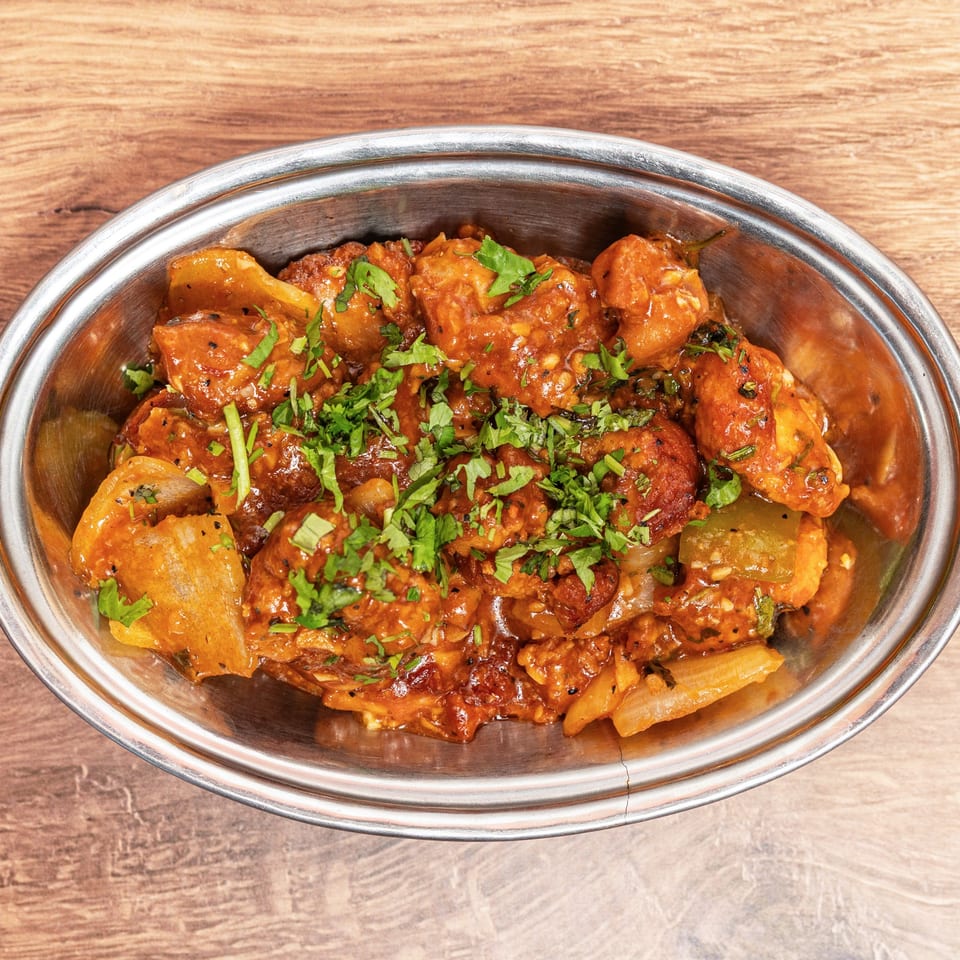 Metal serving dish filled with saucy roasted vegetables and paneer, garnished with fresh cilantro on a wooden table.