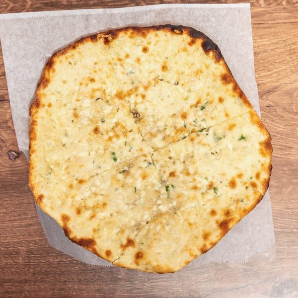 Large golden, herb-speckled flatbread with browned edges, served on parchment over a wooden table.