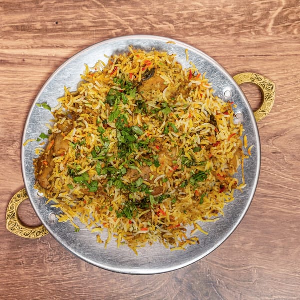 Overhead view of chicken biryani with spiced basmati rice and fresh cilantro on an ornate metal serving platter.