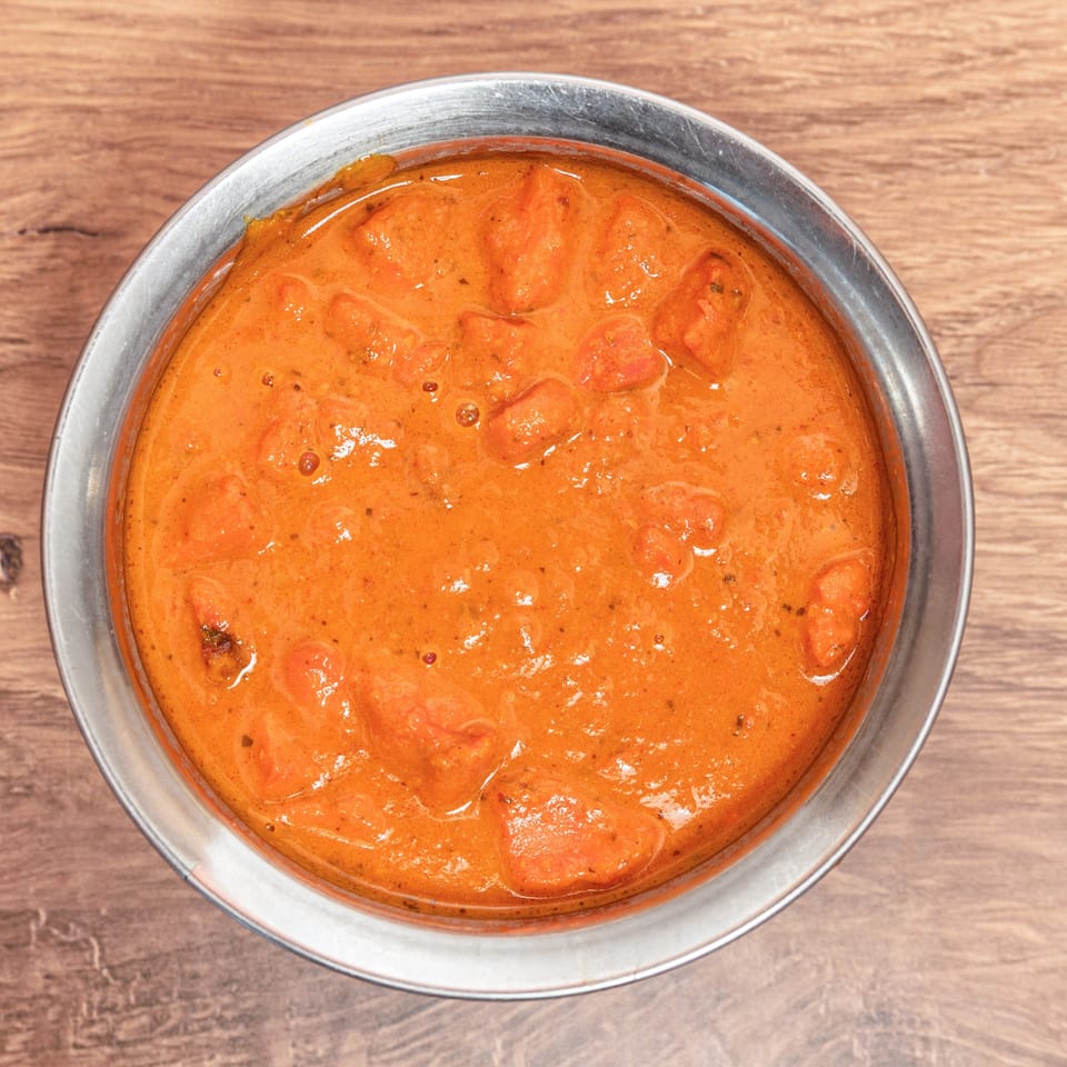 Overhead view of creamy orange curry with chunky pieces served in a metal bowl on a wooden table.
