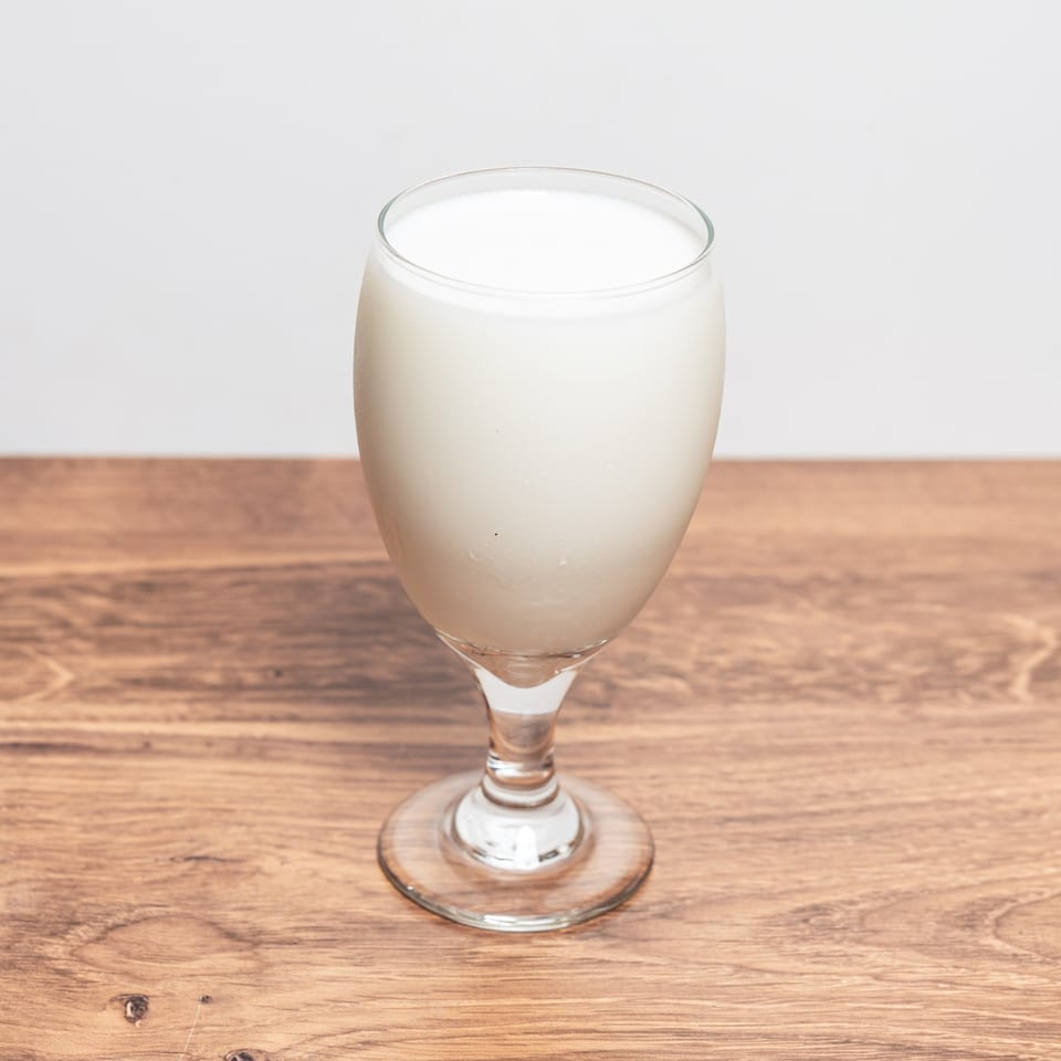 A glass goblet filled with a creamy white beverage sits on a wooden table.