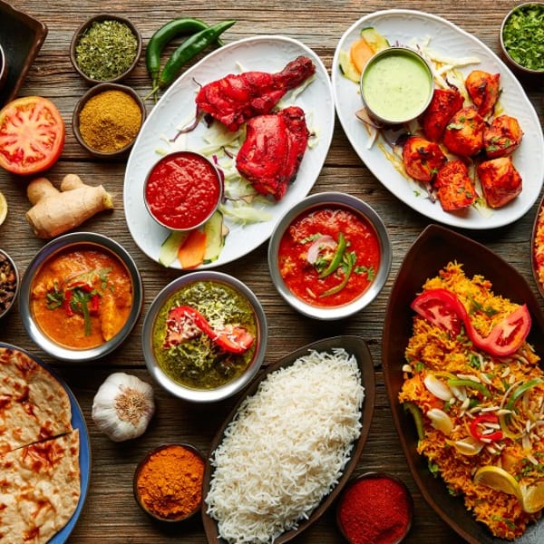 Overhead view of a wooden table laden with various colorful Indian dishes, spices, and ingredients.