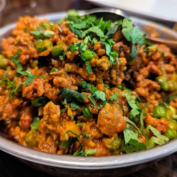 Keema Matar, a vibrant Indian dish with minced meat and peas, garnished with fresh cilantro in a metal bowl.