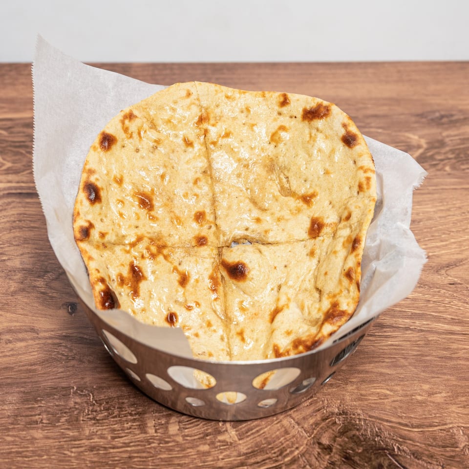 Stack of golden, blistered flatbreads served in a lined metal basket on a wooden table.