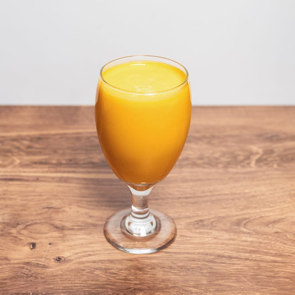 Bright orange drink served in a stemmed glass on a wooden table.